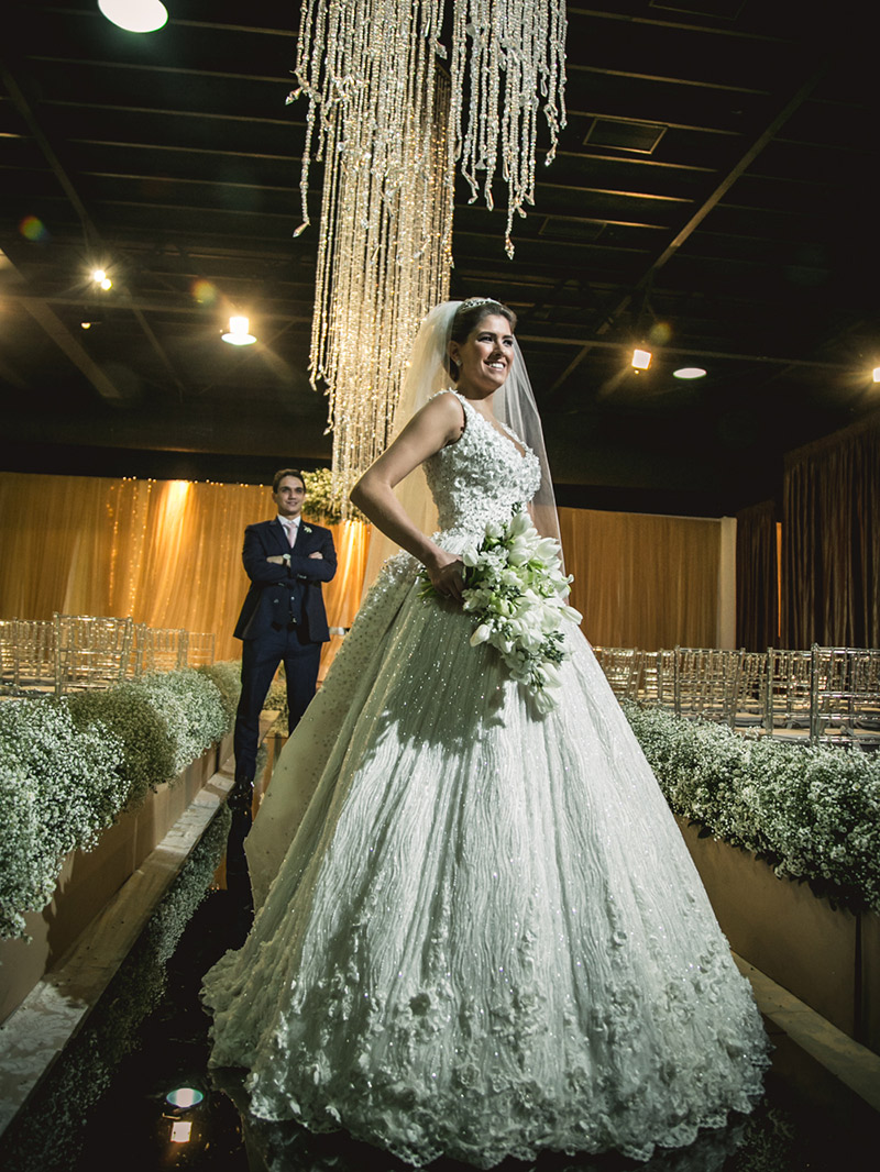 Vestido de noiva posando para foto com noivo ao fundo