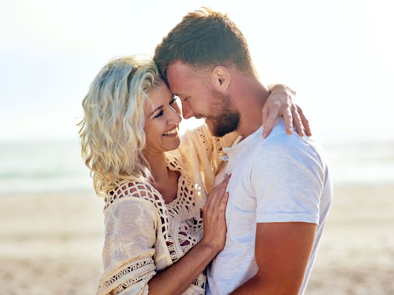 Bodas de algodão - um homem e uma mulher na praia se abraçando e sorrindo