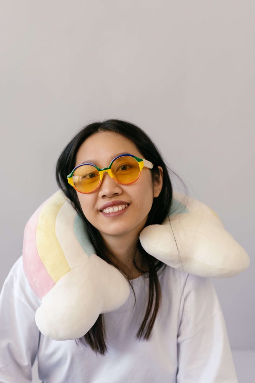 Mulher asiática usando almofada de pescoço e óculos de sol.