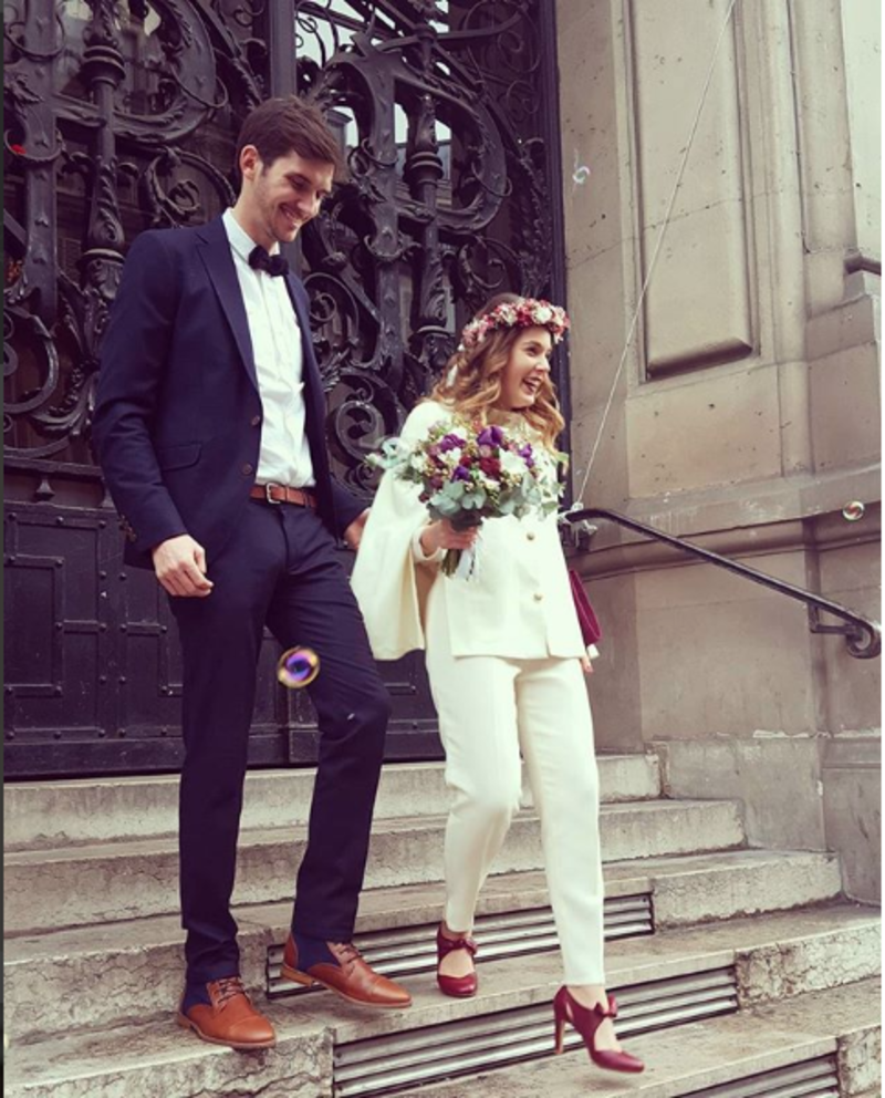 Casal saindo da igreja, a noiva de calça e blusa brancas e sapatos vermelhos e o noivo de terno