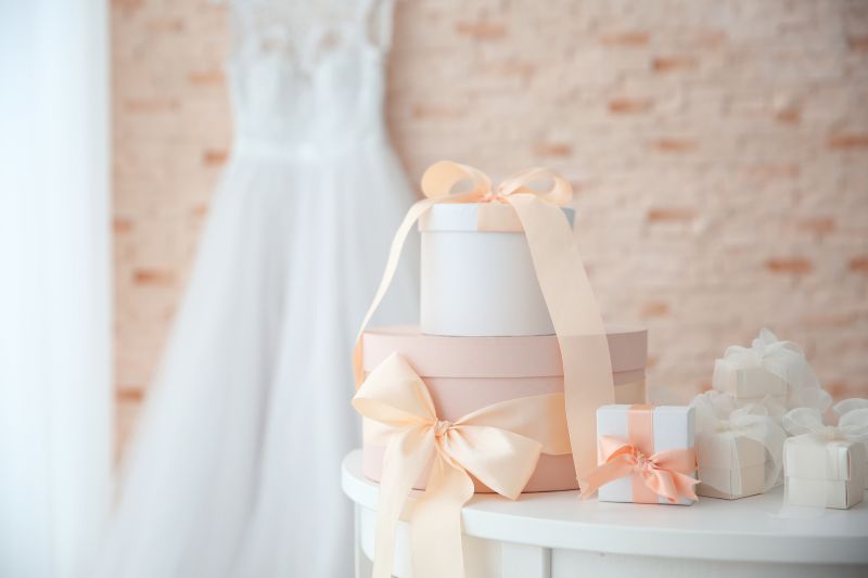 Imagem com presentes de casamento embrulhados e ao fundo um vestido de noiva