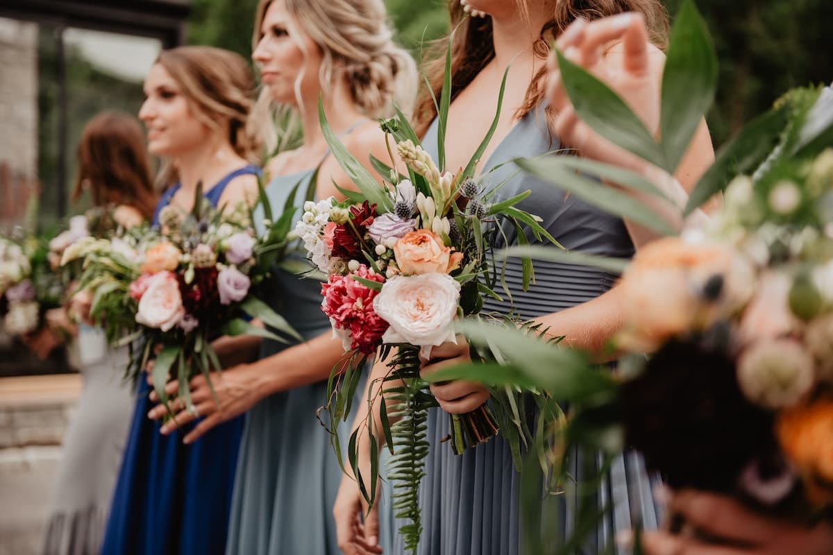 Madrinhas usando vestidos de tons diferentes de azul segurando flores coloridas