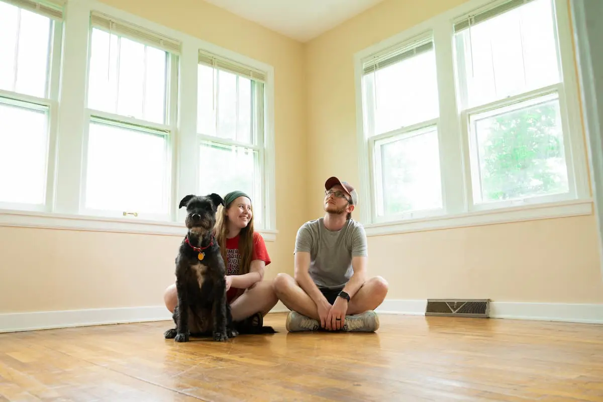 Casal, com seu cachorro de estimação, sentados no chão de sua casa nova.