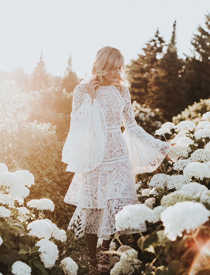 Mulher branca e loira, vestida de noite em um campo de rosas brancas.