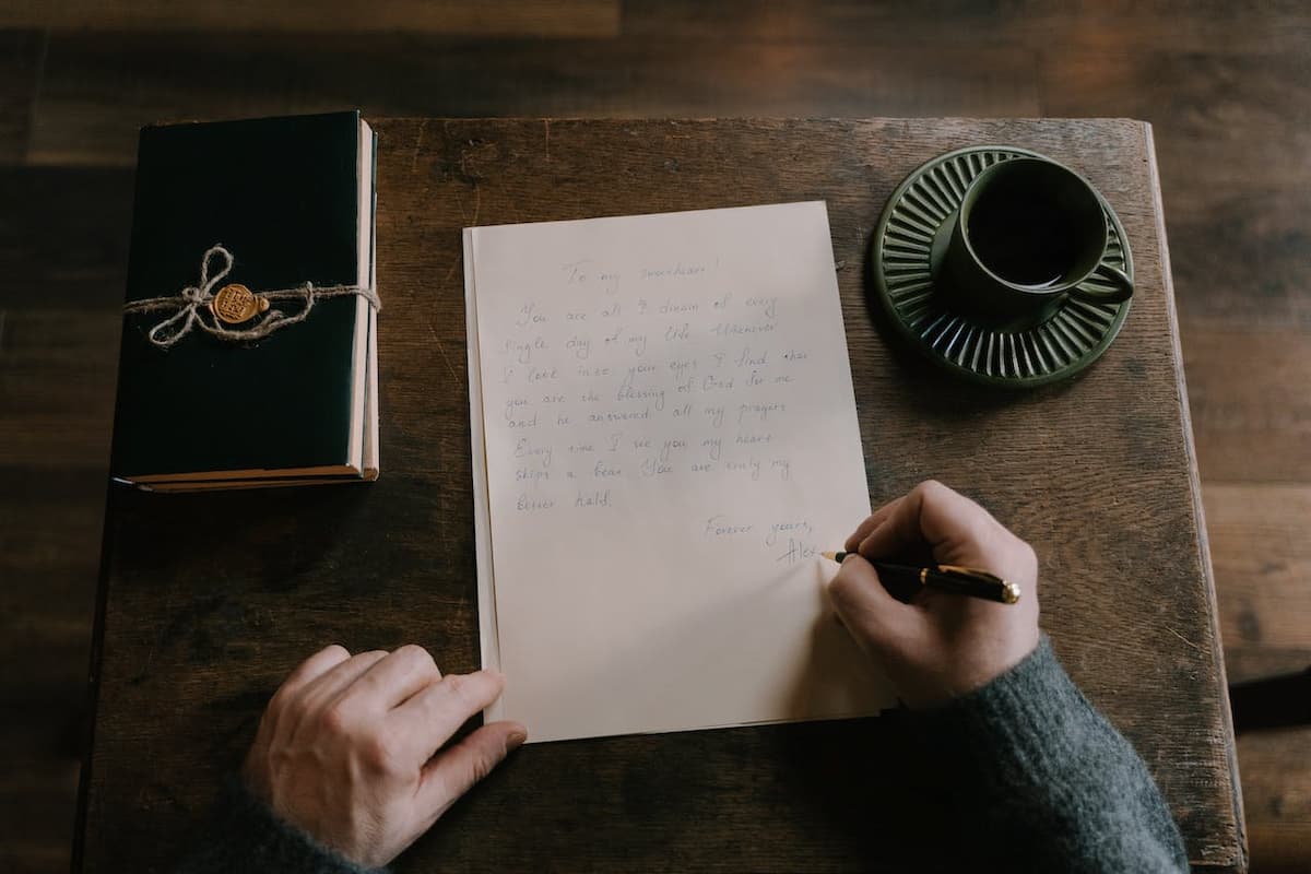 Imagem de um homem escrevendo uma carta em uma mesa de madeira