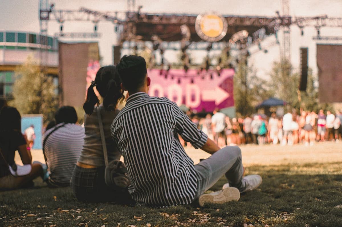 Imagem de um casal sentados na grama esperando um show