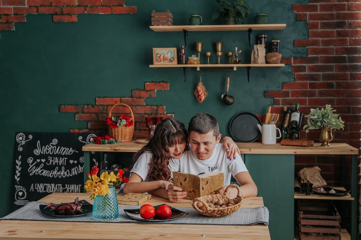 Imagem de um casal lendo um livro de receitas sentados na cozinha