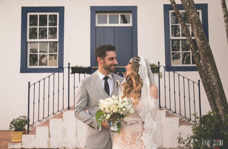 foto de casal recém-casado em frente uma casa com janelas azuis com homem usando terno cinza claro