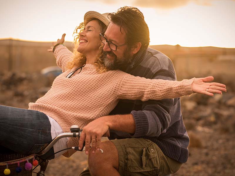 Happy adult people cheerful couple enjoy the outdoor leisure activity riding a bike together man carrying woman and laugh a lot in friendship and relationship - active youthful persons