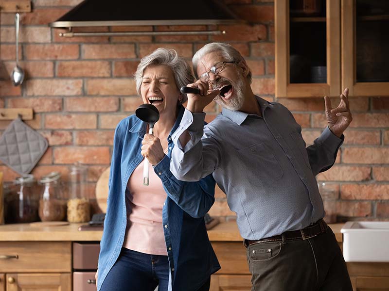 Happy senior husband and wife have fun sing in kitchen appliances cooking together at home. Overjoyed mature grey-haired Caucasian couple feel energetic active enjoy family retirement weekend.