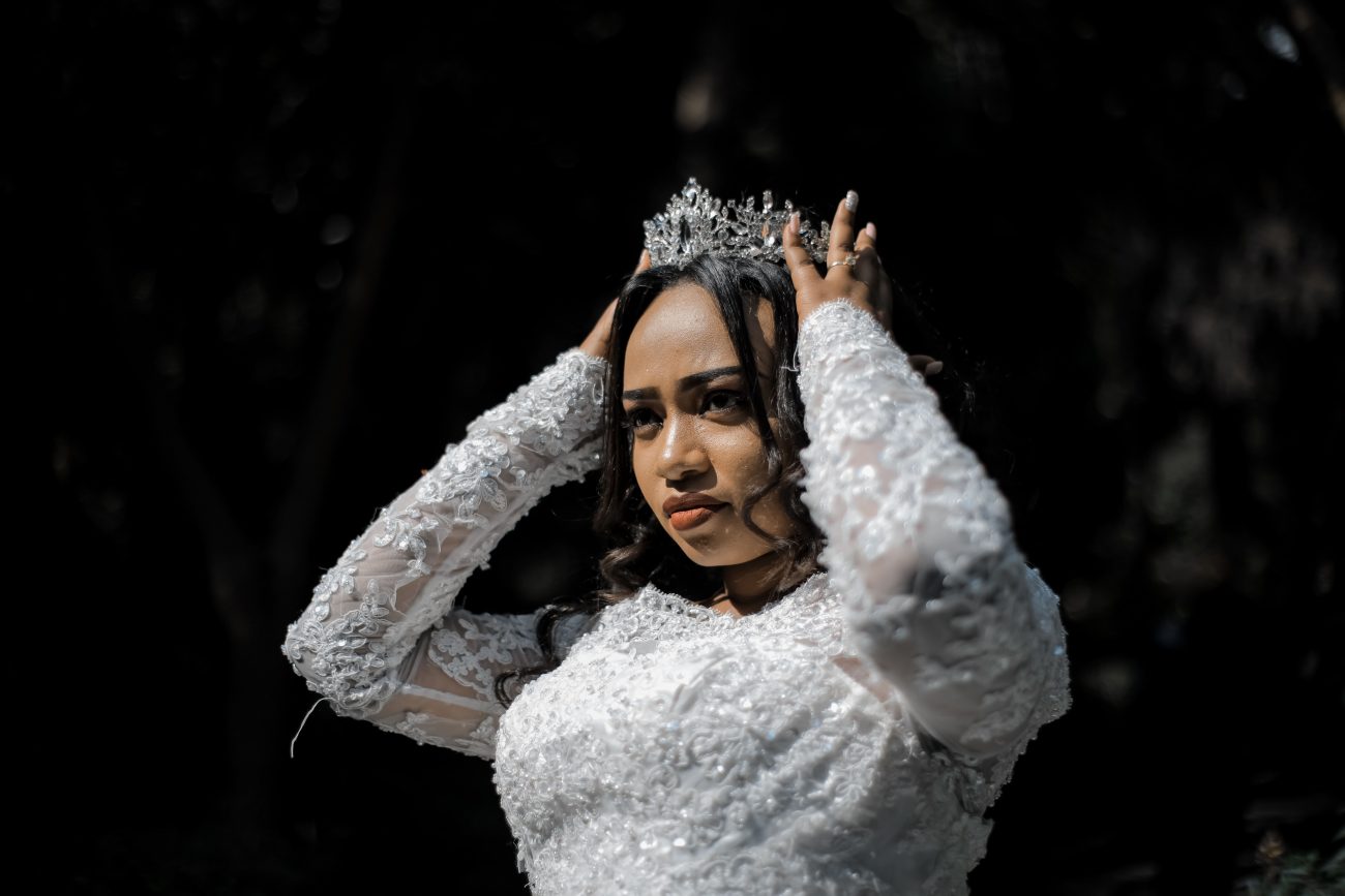Noiva, vestida de branco, coloca uma coroa na cabeça. Imagem disponível em Pexels.