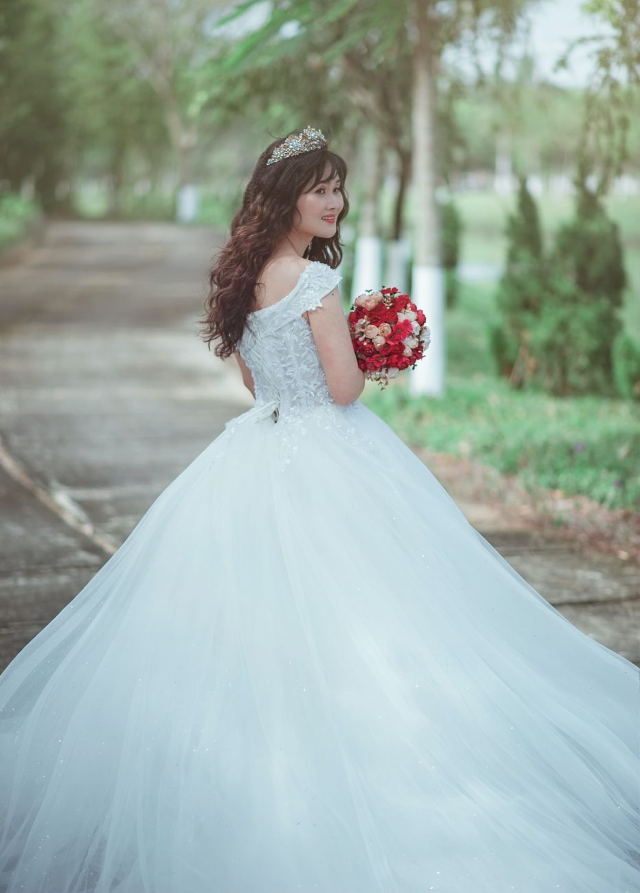 Mulher com vestido de noiva segura um buquê com flores vermelhas. Imagem disponível em Pexels.