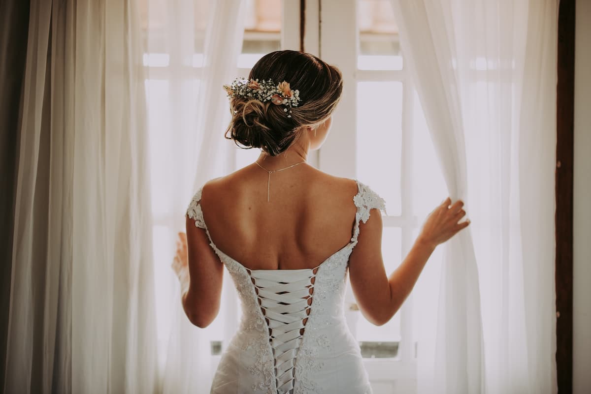 Mulher de vestido de noiva olhando pela janela