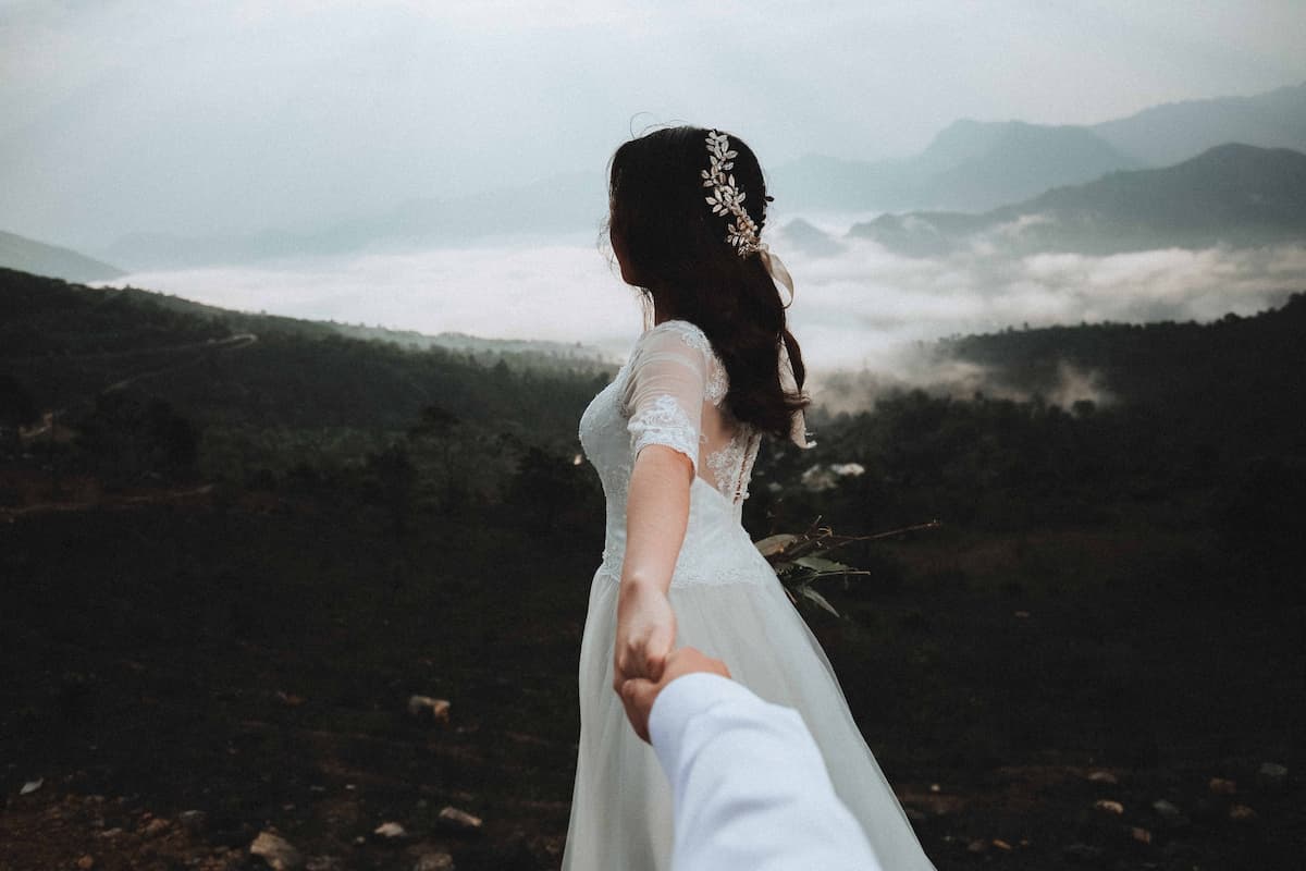 Mulher vestida de noiva em uma montanha segundo a mão de uma pessoa