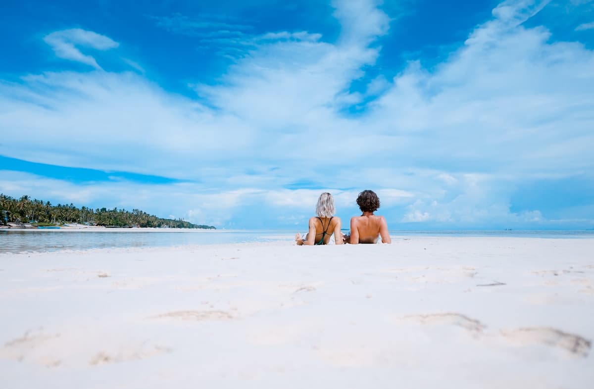 Duas pessoas deitados na areia branca de uma praia durante o dia