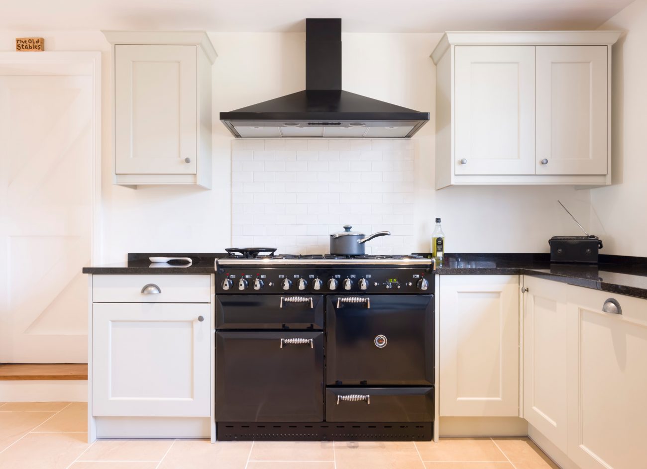 cozinha com depurador de ar, armários brancos e forno preto
