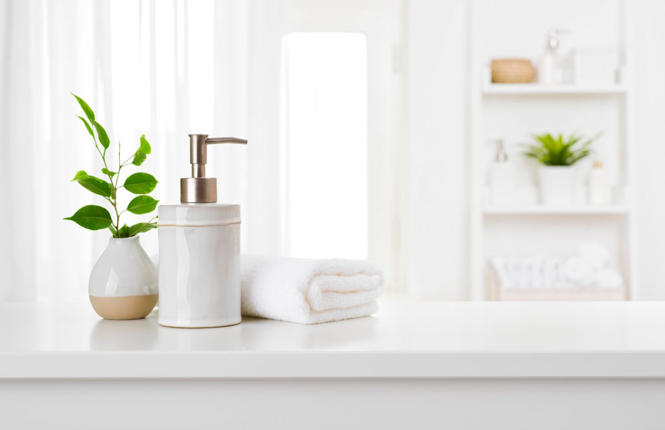 Imagem mostra banheiro, com toalha branca, e vidro de sabonete liquido 