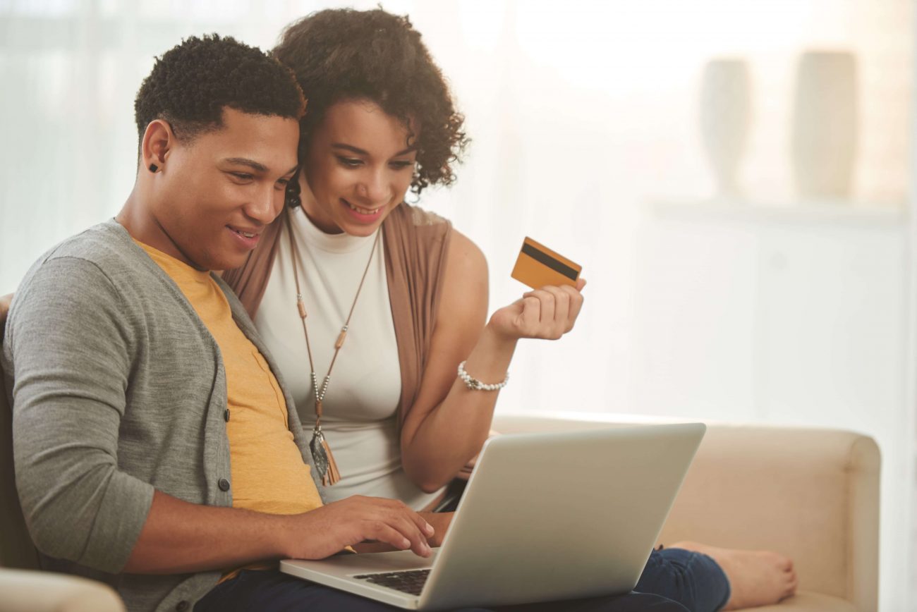 Homem e mulher na frente do computador segurando o cartão de crédito
