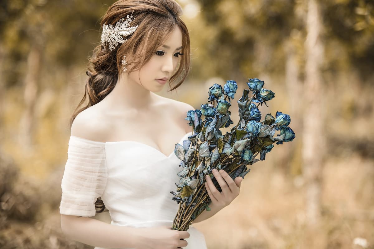 Imagem de uma noiva com vestido de manga segurando um buquê com flores azuis