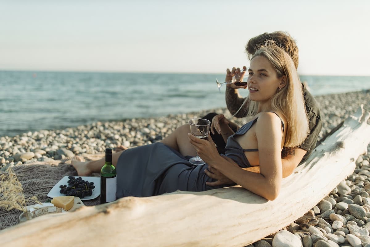 Casal deitado na praia bebendo vinho