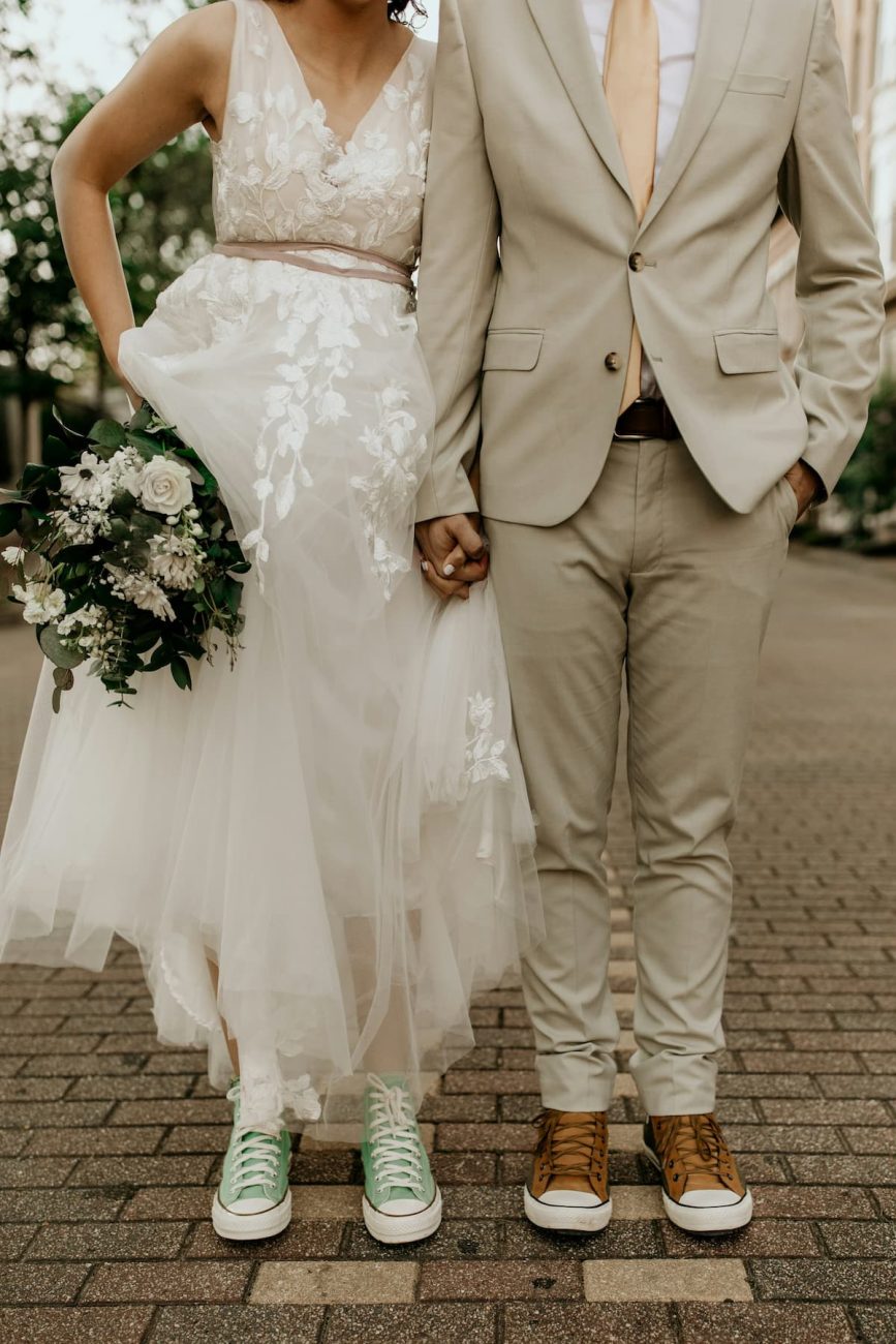 Imagem de um casal de mãos dadas com trajes de casamento