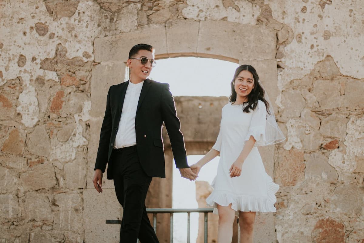 Imagem de um casal sorrindo caminhando com a mulher usando um vestido de noiva curto