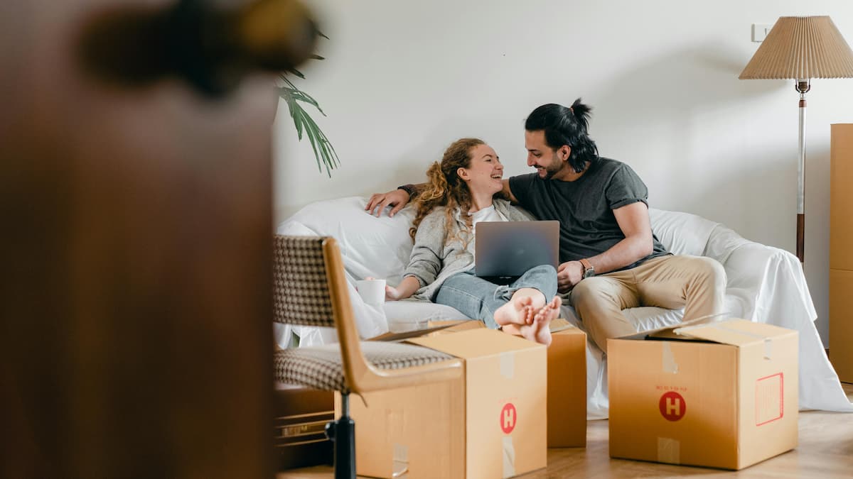 Um casal em seu apartamento com caixas e um computador na mão