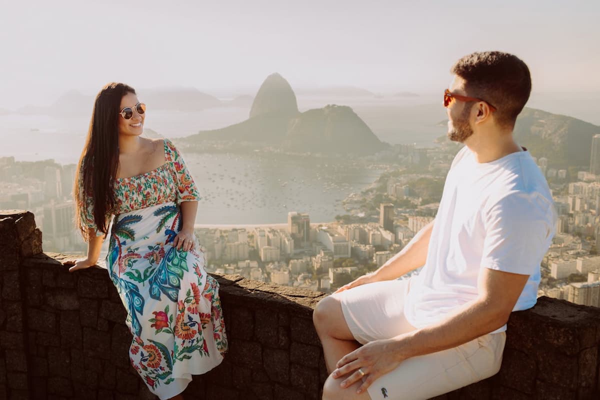 Imagem de um casal sentado em um mirante com uma paisagem no fundo