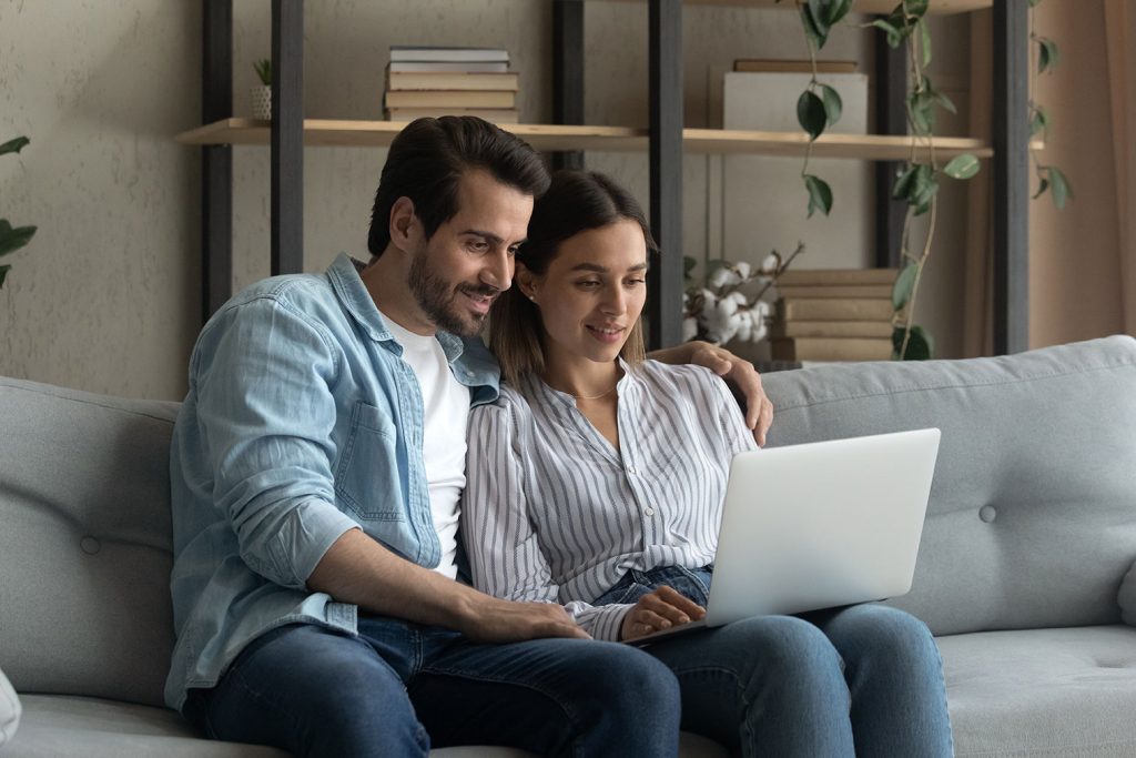 Casal sentados juntos em sofá e mexendo no notebook.
