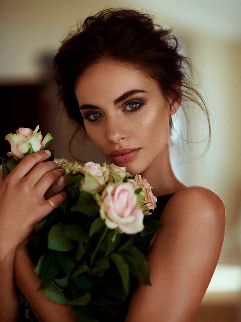 Mulher com cabelo preso e levemente bagunçado, segurando um buquê de rosas. Maquiagem para casamento de dia.