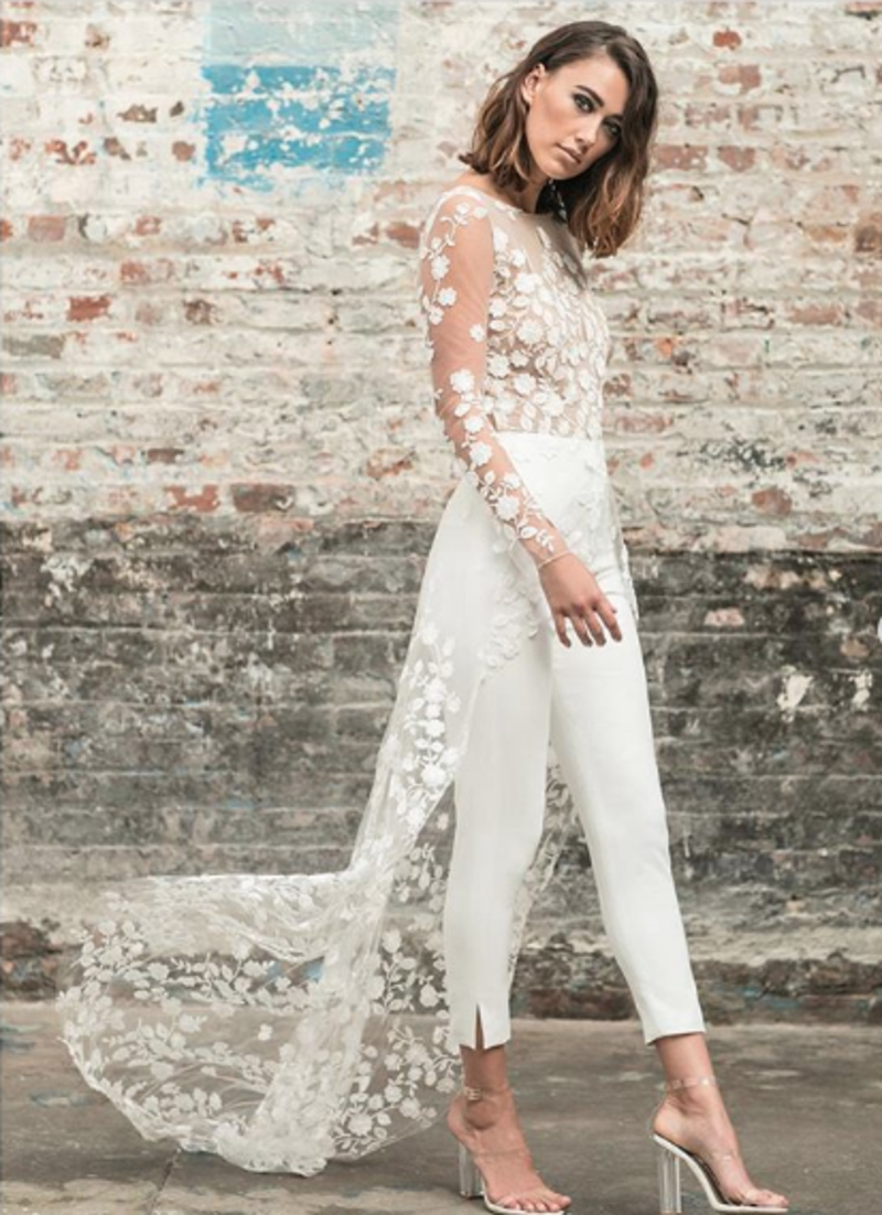 noiva de calça e uma blusa com detalhes florais e cauda longa.