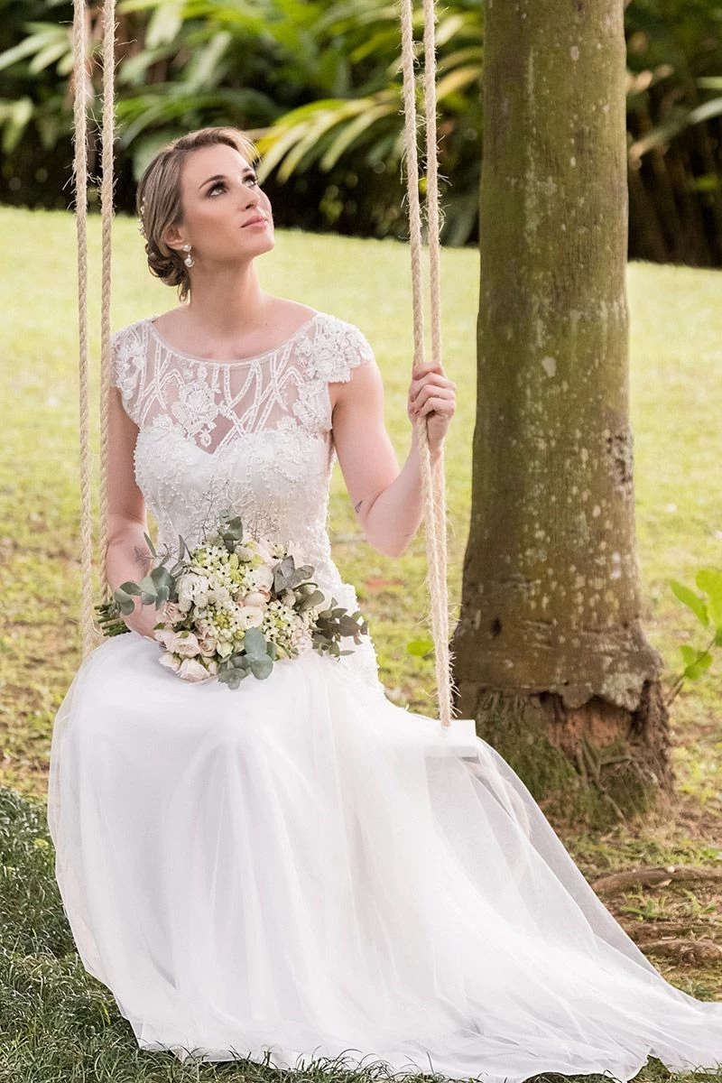 Vestido de noiva para casamento no campo modelo sentada no balanço com vestido com transparência renda e mangas