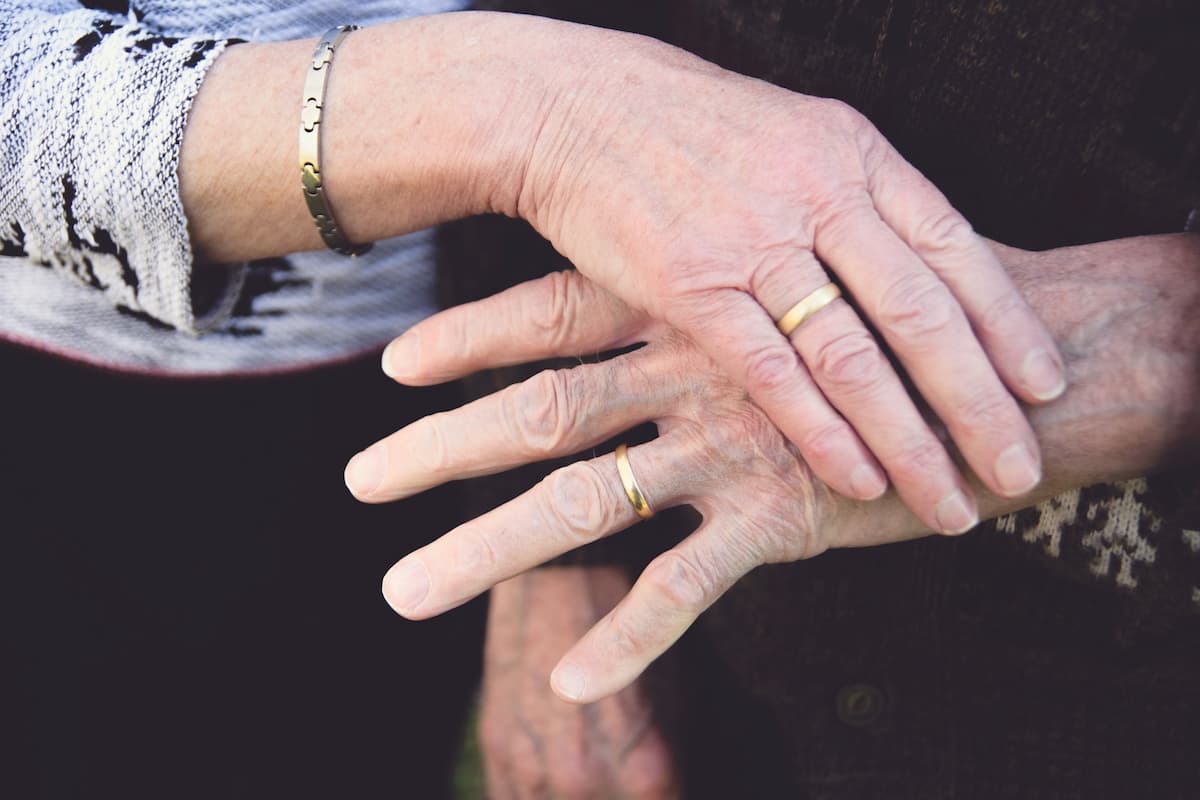 Bodas de casamento: imagem das mãos de dois idosos casados|Bodas de casamento: imagem de duas pessoas sentadas de frente para o mar