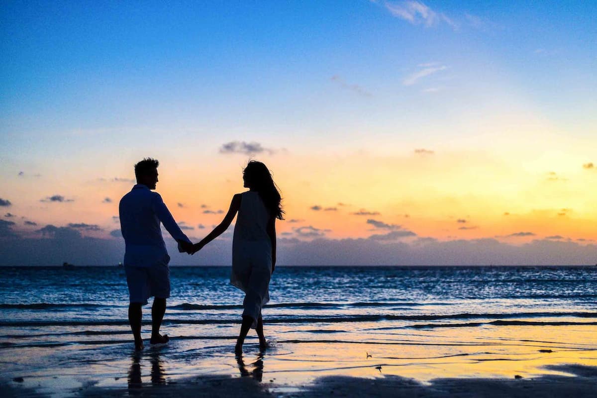 Casal de mãos dadas passeando na praia no pôr do sol|||1 ano de casamento