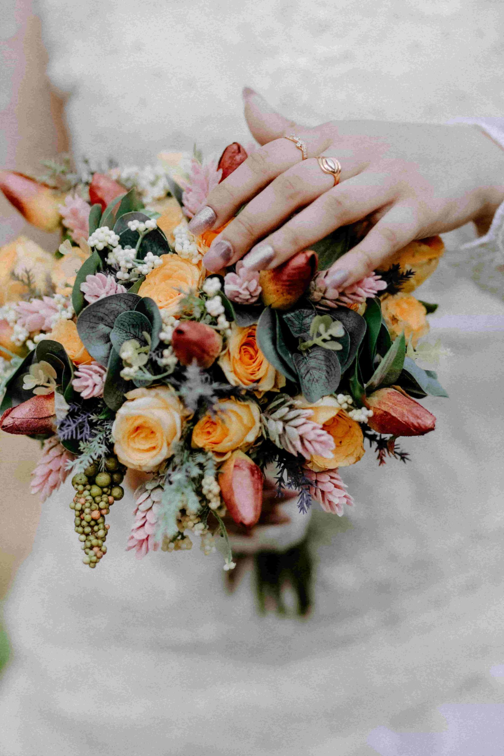 Buquê de noiva colorido em tons quentes, incluindo flores vermelhas, laranjas e amarelas.