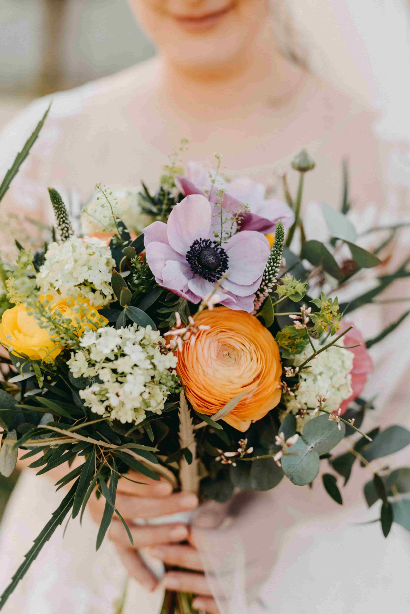 Noiva segurando um buquê de noiva colorido com tons de rosa, amarelo e verde.