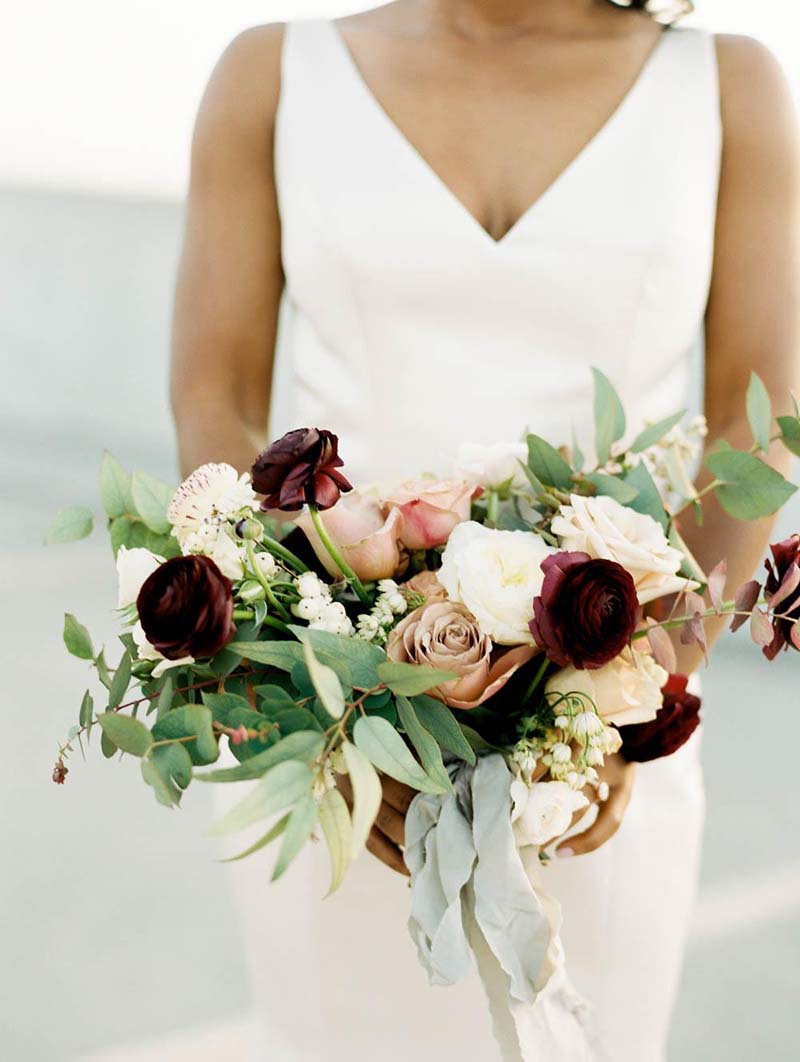 Noiva com vestido de noiva off white e buquê de noiva com muitas folhagens e flores vermelhas e brancas, foto Renee Hollingshead Photography