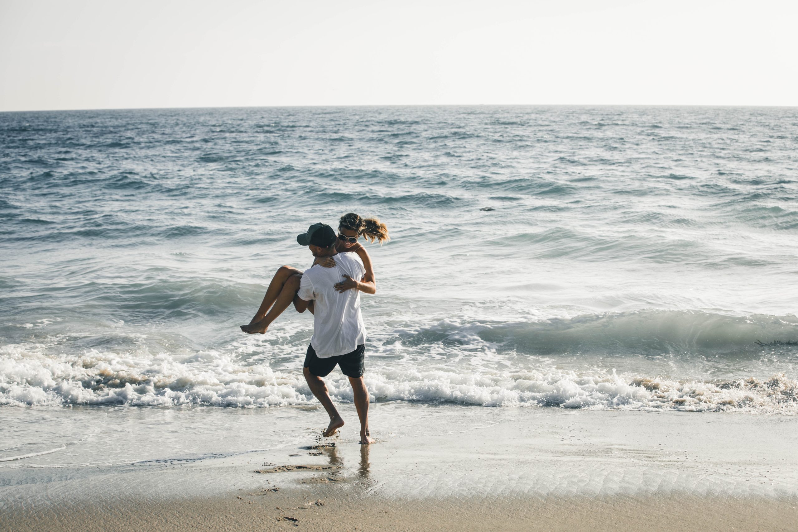 Como planejar lua de mel: casal aproveitando a praia. A imagem mostra um casal em um momento romântico de abraço, desfrutando da paisagem de uma praia paradisíaca.