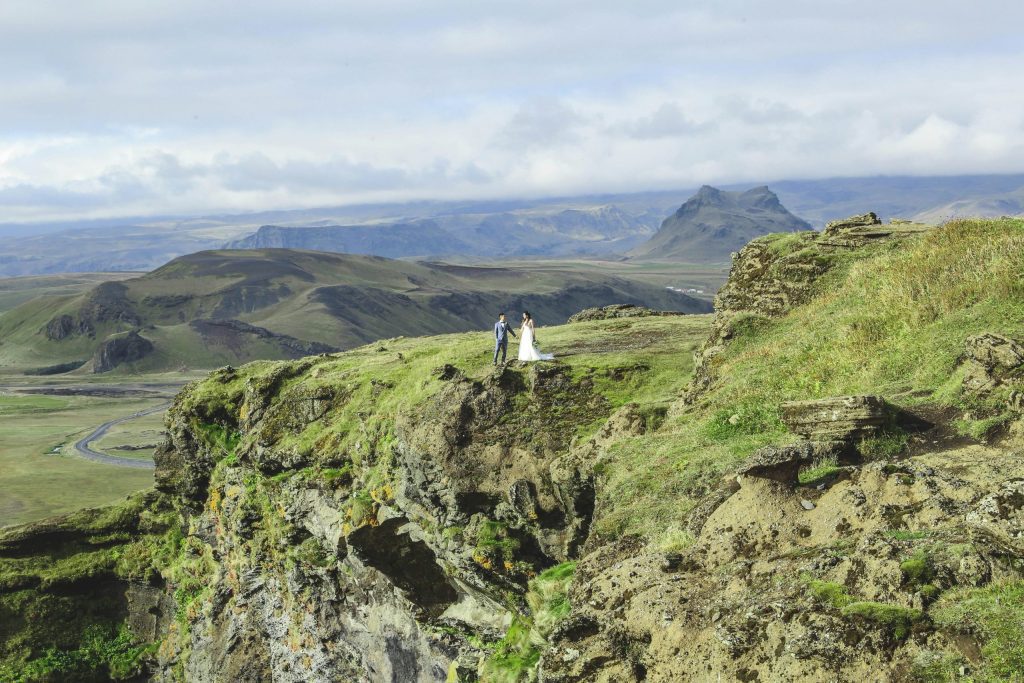 Foto panorâmica de casal em montanha com céu azul|Casal de noivos posa para foto em cenário bucólico na montanha