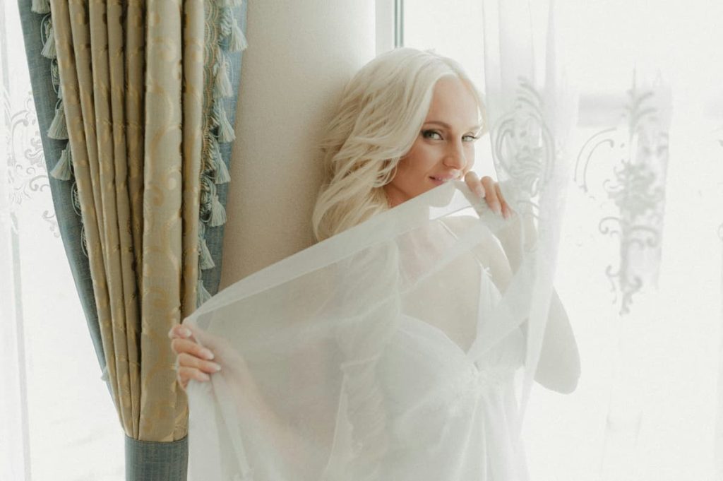 Uma mulher de lingerie atrás da cortina|noiva-com-lingerie-branca-com-renda|noiva-com-espartilho-branco|noiva-com-lingerie-com-renda|lingerie-para-noivas-de-cor-nude-rosada|noiva-com-sutia-branco-com-renda|noiva-com-camisola-vermelha-de-seda|Lingerie para noivas o que usar por baixo do vestido|Lingerie para noivas o que usar na lua de mel|Lingerie para noivas o que usar na lua de mel|Lingerie para noivas o que usar por baixo do vestido|Uma mulher deitada na cama de barriga para baixo