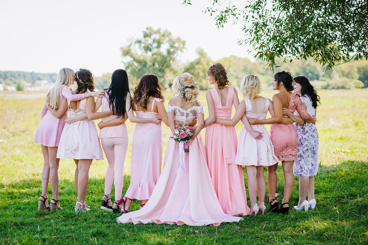 Imagem de uma noiva e suas madrinhas com vestidos rosa|convidadas-com-vestidos-de-festa-coloridos|vestido-de-festa-estampado-com-flores|vestido-de-festa-cromado|vestido-de-festa-midi-estampado|vestido-de-festa-preto-curto|vestido-de-festa-midi-verde-esmeralda|vestido-de-festa-nude|vestidos-de-festa-estampados|||Imagem de uma mulher com vestido estampado em um lugar com flores lilás|Imagem de um vestido de renda branco pendurado na parede|Imagem de um vestido vermelho em um manequim longo e com brilhos|Imagem de uma mulher com vestido curto rosa|Mulher com vestido longo preto em uma grama alta|