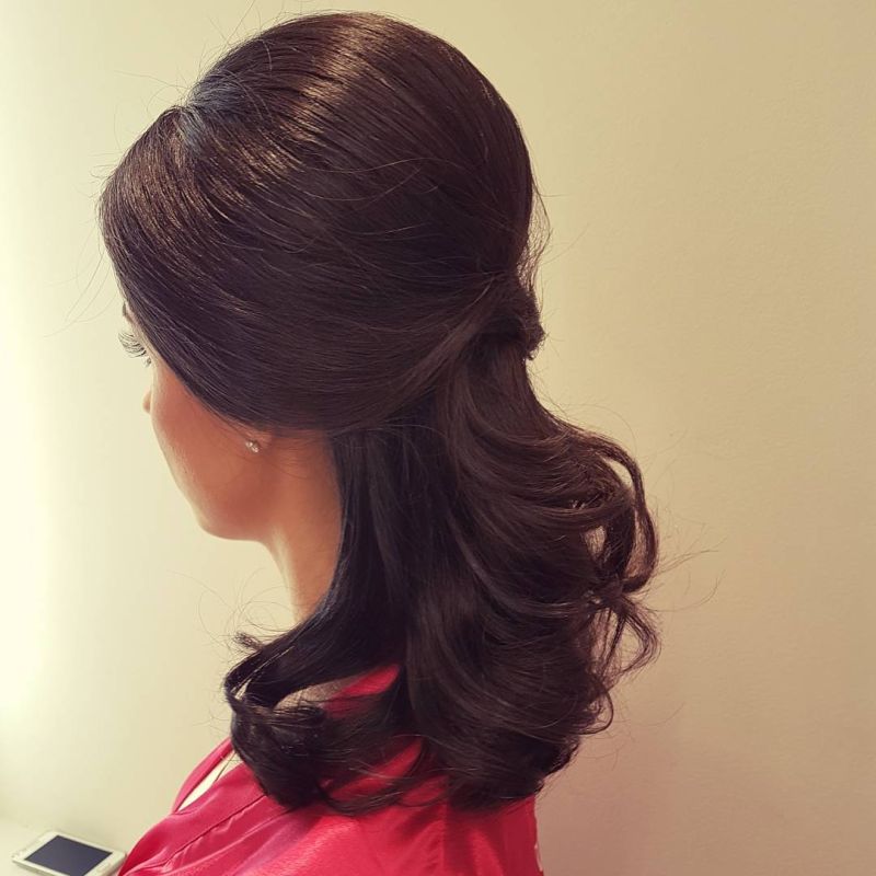 Madrinha de casamento de cabelos escuros exibe penteado semi solto frente ao fundo amarelado.