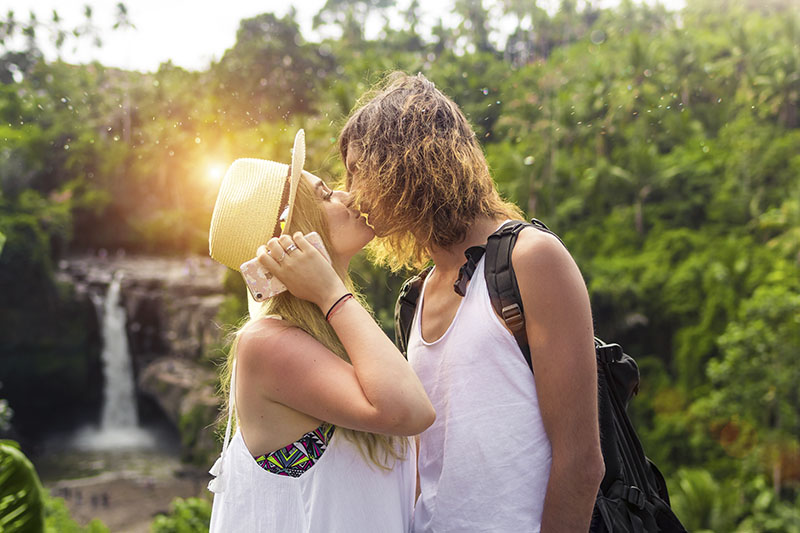 Como planejar lua de mel: casal se beijando na cachoeira. Um casal em um momento romântico de beijo em frente a uma cachoeira em meio à natureza.