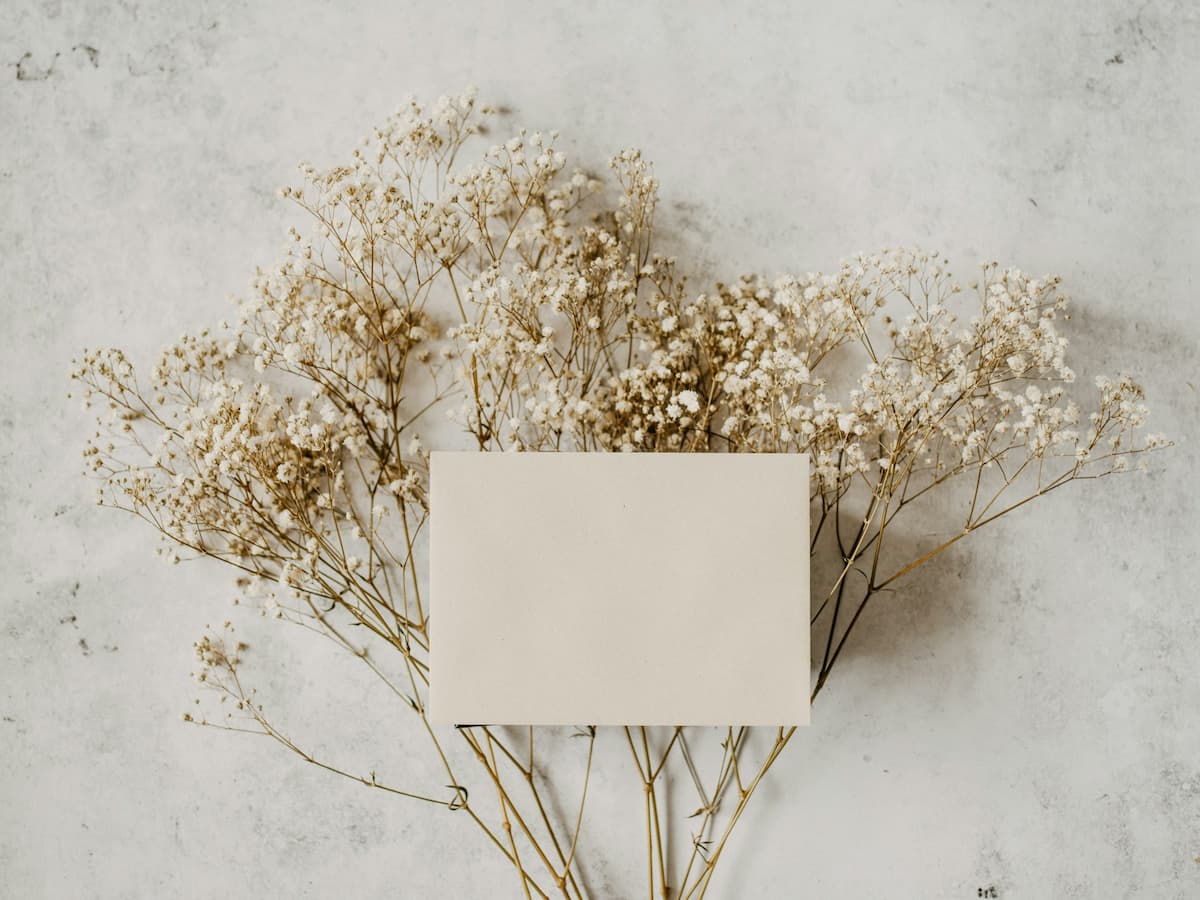 Imagem de um cartão em branco em cima de flores brancas|Imagem de um conjunto de xícaras|Imagem de um casal sentados no sofá assistindo televisão|Imagem de um porta-retrato dourado do lado de um vaso com uma rosa|Imagem de um livro de receitas em cima da mesa da cozinha|Imagem de um vaso de flores|Imagem de um vinho