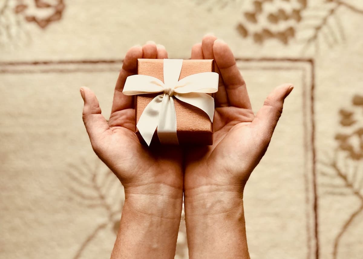 Imagem de uma pessoa segurando uma caixa de presente pequena com o papel rosa claro|Imagem de um casal andando dentro do museu com uma exposição de múmias|Imagem de um casal assistindo televisão|Imagem de um assistente virtual branco em cima da mesa|Imagem de um casal dançando no pôr do sol|Imagem de uma câmera analógica em cima de uma mesa com filmes do lado|Imagem de um quarto com uma cama ao fundo com uma mesa na frente com champanhe e doces|Imagem de uma mulher segurando uma câmera tirando foto|Imagem de utensílios de pintura|Imagem de um casal sentado em um restaurante com cadeiras vermelhas|Imagem de um casal sentado em um mirante com uma paisagem no fundo|Imagem de uma caixa de presente azul em um fundo branco