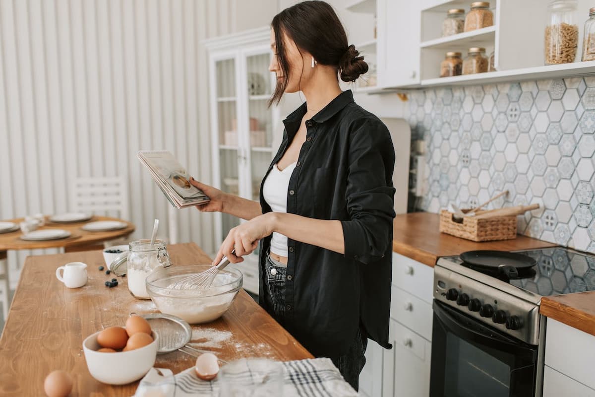 Mulher cozinhando em sua casa lendo um livro de receitas